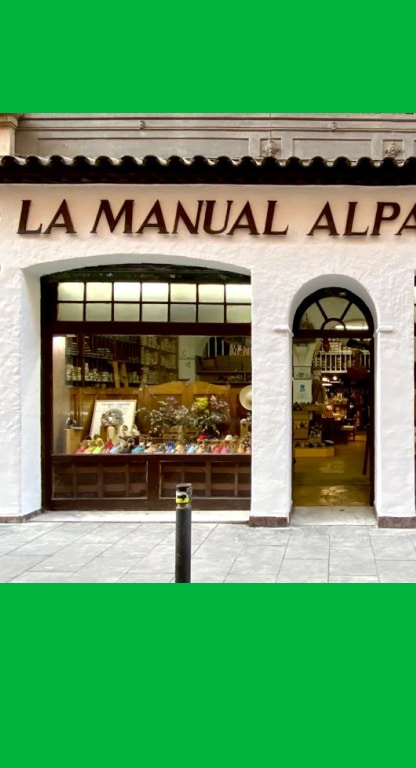 Facade of La Manual Alpargatera Barcelona espadrilles shop. Wooden sign with the name of the brand, adorned with vintage plates on the sides, two sideboards and a central door, all painted white with brown wooden details