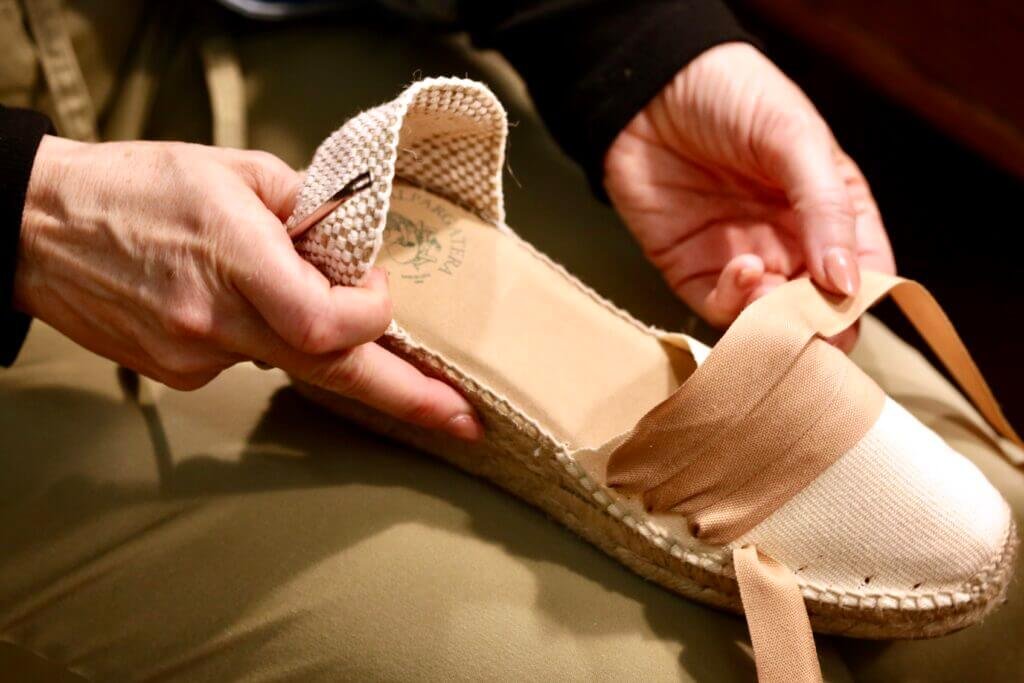 Manos encintando una alpargata artesanal durante una experiencia tradicional de elaboración de alpargatas en Barcelona